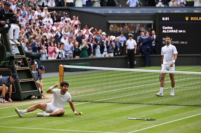 Petenis Spanyol, Carlos Alcaraz (kiri), merayakan kemenangannya atas Novak Djokovic dari Serbia pada final tunggal putra Wimbledon 2023 di The All England Tennis Club, London, Inggris, Minggu (16/7/2023). (Foto: AFP PHOTO)