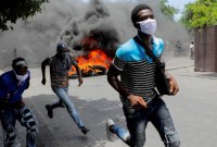 Tiga orang pria berlari di samping ban yang terbakar selama protes menuntut diakhirinya kekerasan geng, di Port-au-Prince, Haiti, Senin, (14/8/2023) waktu setempat. (REUTERS/Ralph Tedy Erol)
