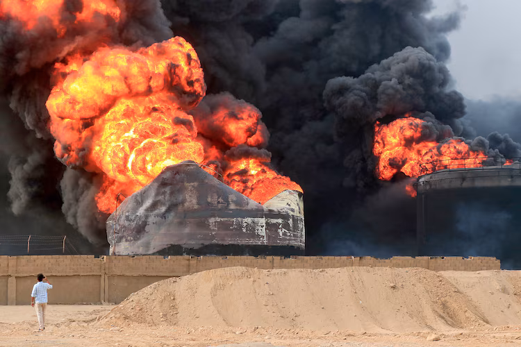 Seorang pria mengambil gambar api yang berkobar di tangki penyimpanan minyak sehari setelah serangan Israel di pelabuhan kota Hodeida yang dikuasai Huthi di Yaman pada Minggu (21/7/2024). [AFP via Getty Images]