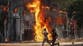 Pria berlari melewati pusat perbelanjaan yang dibakar oleh pengunjuk rasa selama unjuk rasa menentang Perdana Menteri Sheikh Hasina, 4 Agustus 2024. (AP Photo/Rajib Dhar)
