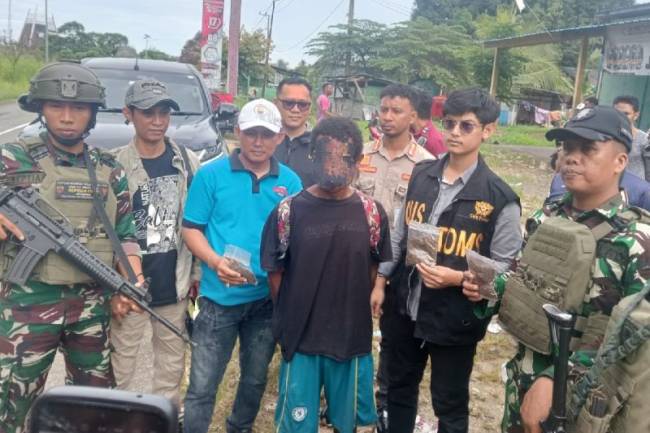 
Tim gabungan TNI-Polri beserta Bea Cukai dan Imigrasi menangkap JK (tengah), warga negara Papua Nugini (PNG), yang membawa 12 paket ganja, di Pos Lintas Batas Negara (PLBN) Skouw, Jayapura, Papua, Minggu (9/2/2025). (ANTARA/HO-Polresta Jayapura Kota)