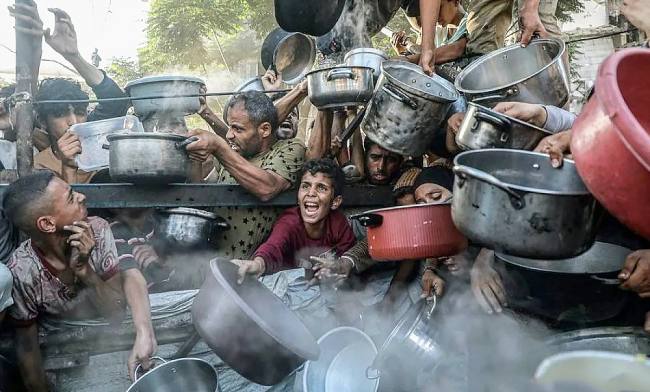 Seorang anak bersama pengungsi lainnya menunggu pembagian makanan gratis dari pusat distribusi makanan di Kota Gaza, Palestina (14/7/2025). (Xinhua/Rizek Abdeljawad)