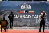 Petugas keamanan berada di dekat baliho perundingan AS-Iran di luar pusat media di Islamabad, Pakistan, Minggu (12/4/2026). (AP/ANJUM NAVEED)