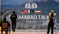 Petugas keamanan berada di dekat baliho perundingan AS-Iran di luar pusat media di Islamabad, Pakistan, Minggu (12/4/2026). (AP/ANJUM NAVEED)