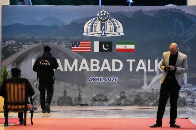 Petugas keamanan berada di dekat baliho perundingan AS-Iran di luar pusat media di Islamabad, Pakistan, Minggu (12/4/2026). (AP/ANJUM NAVEED)