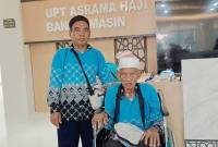 H Kasrun Sahidin Abdullah yang merupakan haji tertua Debarkasi Banjarmasin tahun 1447 H / 2026 M, yakni berusia 101 tahun dan sang anak saat tiba di tanah air pada Kloter 17 di asrama haji di Kota Banjarbaru, Minggu (28/6/2026). (Foto: PPIH Debarkasi Banjarmasin)